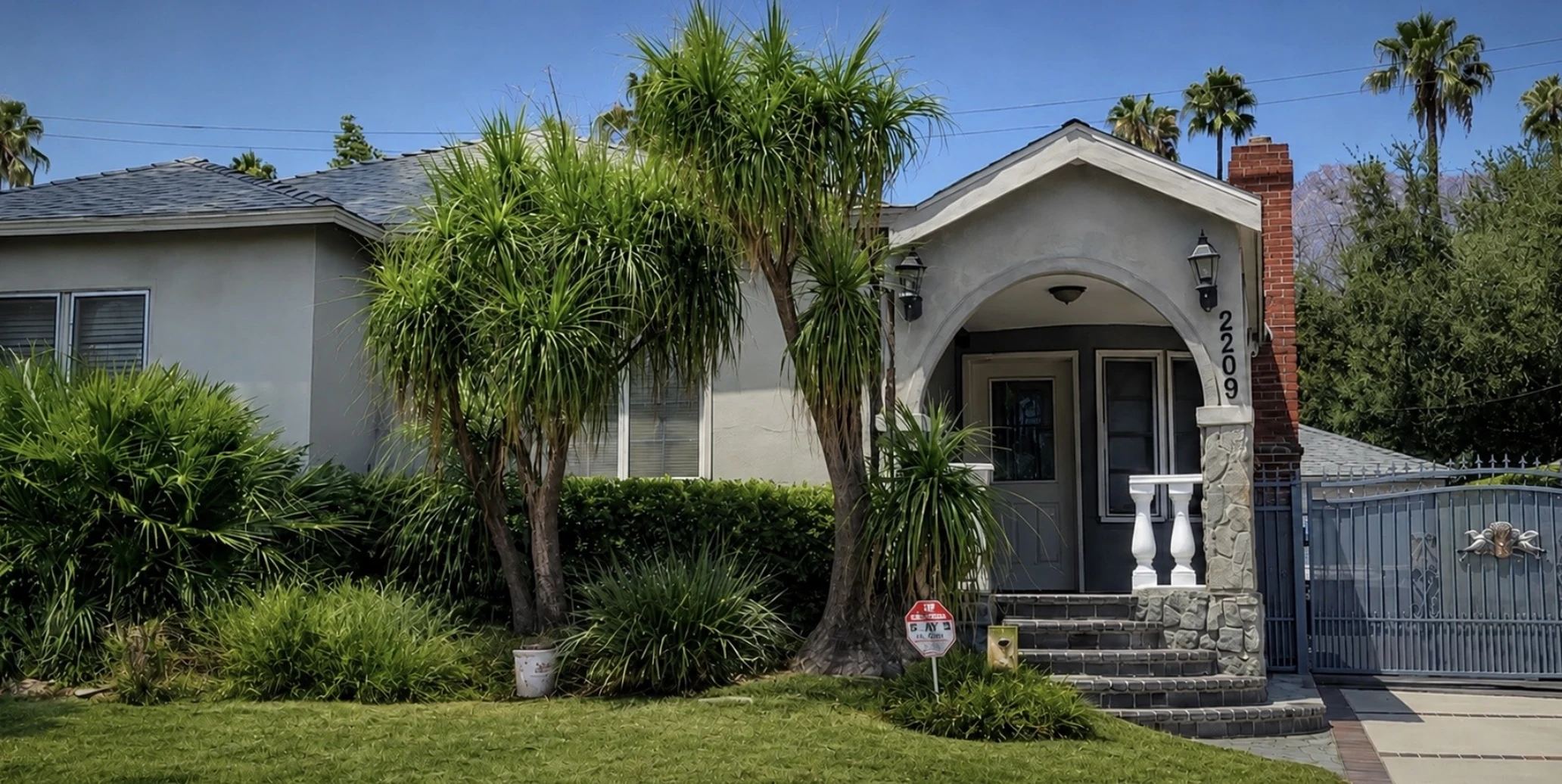 الواجهة الأمامية لمنزل 2209 Queensberry Road، باسادينا، كاليفورنيا 91104، تُظهر مدخل الشرفة المقوّس ورقم 2209 على العمود الحجري والممر المسوّر